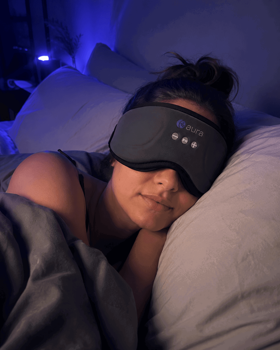 Woman sleeping soundly in a dark room wearing the Aura Sleep Mask
