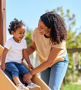 Parent helping their child go down a playground slide