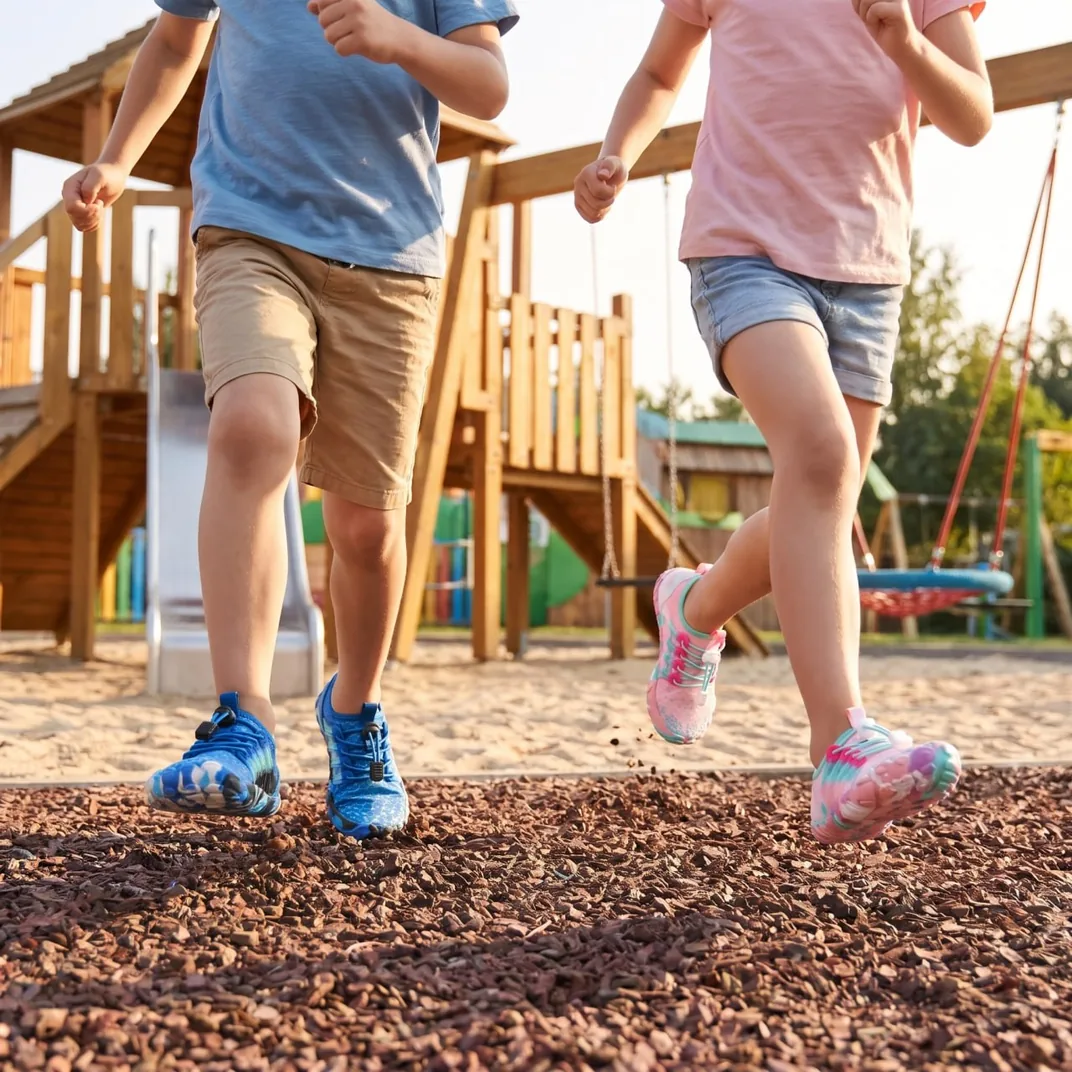 Two kids running on a playground in Grounded Footwear® Freedom Kids