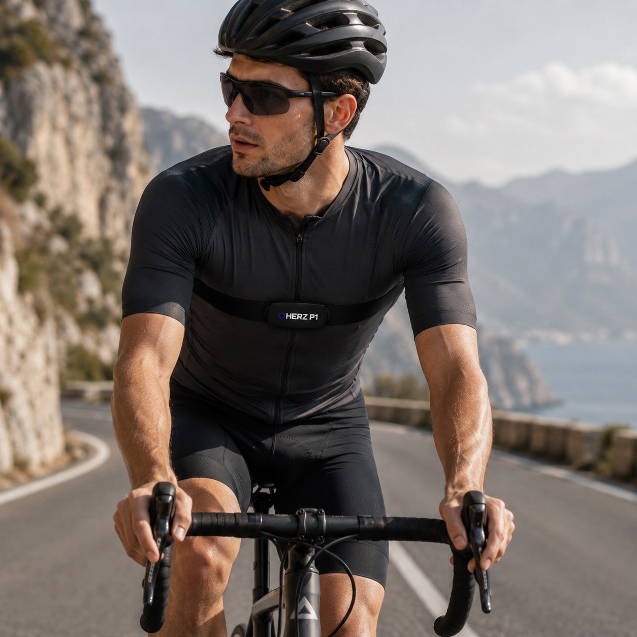 Cyclist riding a road bike along a coastal mountain road wearing the Herz P1 chest strap
