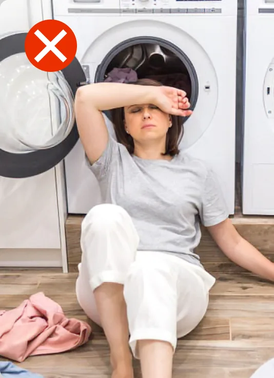 Tired woman surrounded by laundry in front of a washing machine